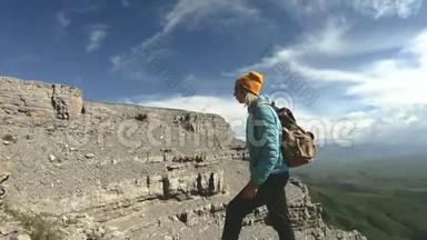 一个带着<strong>双肩包</strong>和太阳镜的微笑的旅游女孩带着她的相机走在一个岩石高原的边缘